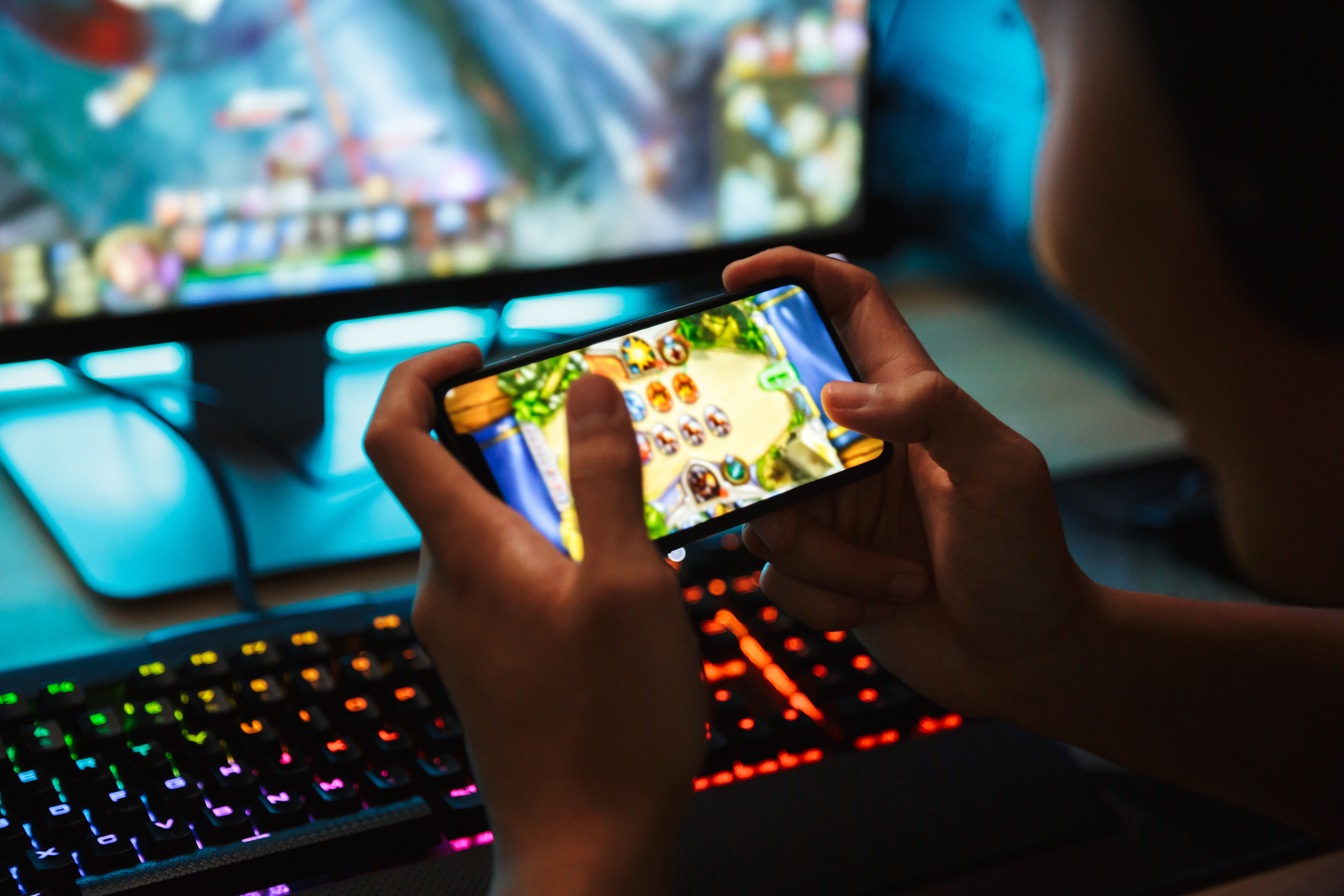 Pessoa acessando jogo online no celular e computador gamer ao fundo